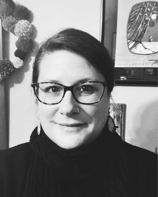 A white woman with glasses and a thoughtful expression leans on a doorframe.