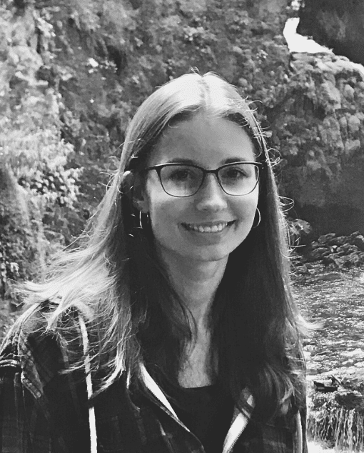 A white woman with glasses and a thoughtful expression leans on a doorframe.