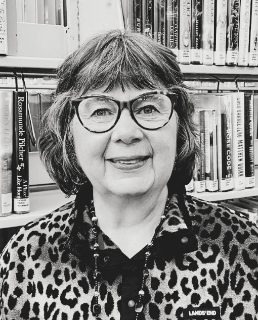 A white woman with glasses and a thoughtful expression leans on a doorframe.