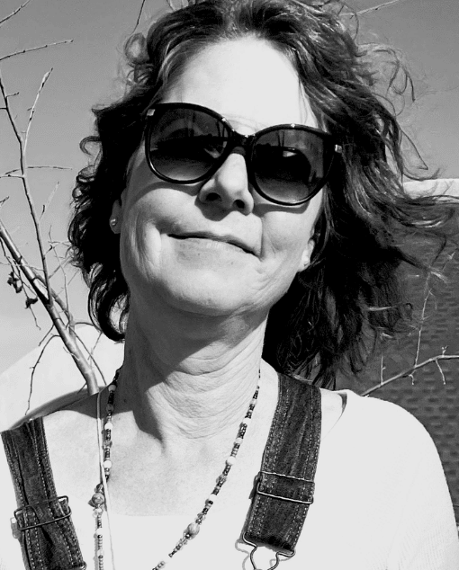A white woman with glasses and a thoughtful expression leans on a doorframe.