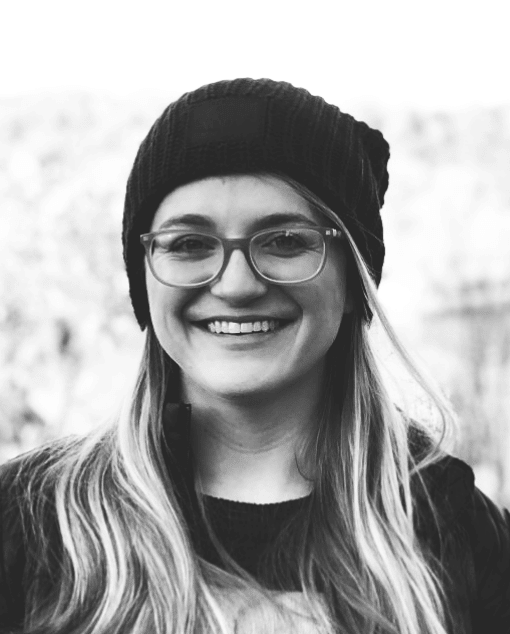 A white woman with glasses and a thoughtful expression leans on a doorframe.